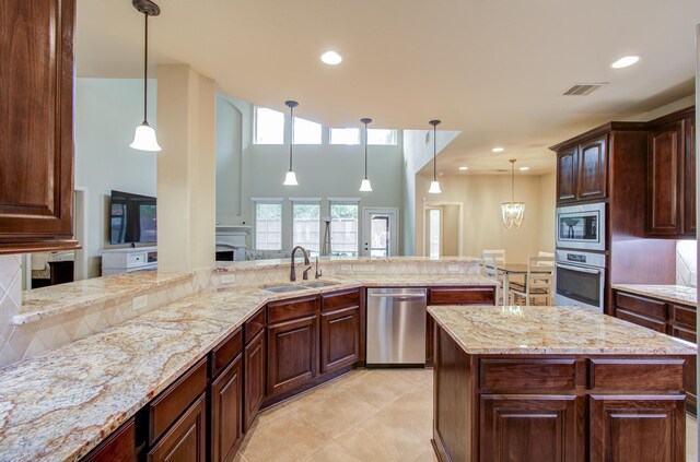 kitchen featuring sink, hanging light fixtures, stainless steel appliances, light stone countertops, and kitchen peninsula