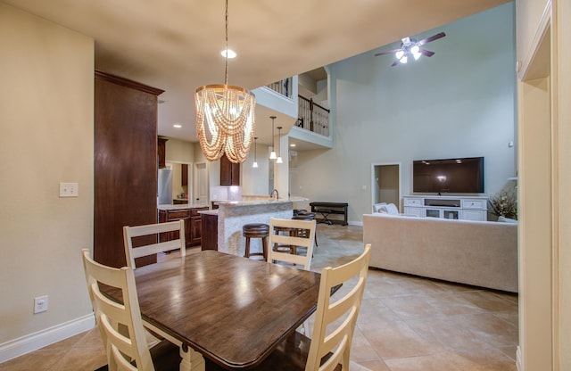 tiled dining area with ceiling fan with notable chandelier and a high ceiling