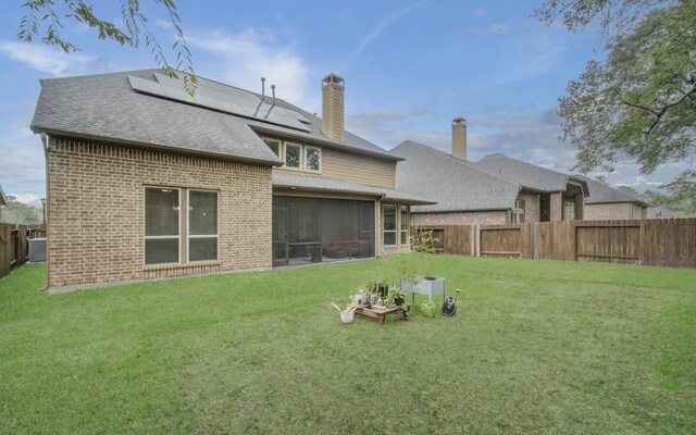 back of property with a yard, a sunroom, and solar panels