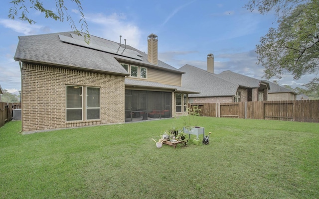 back of property featuring solar panels, a lawn, a sunroom, a fenced backyard, and brick siding