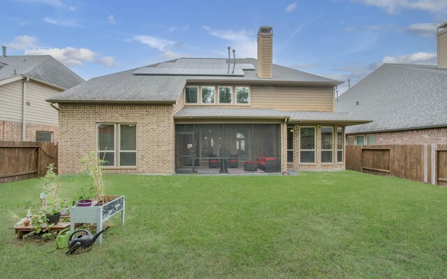 rear view of property featuring a yard, a sunroom, and solar panels