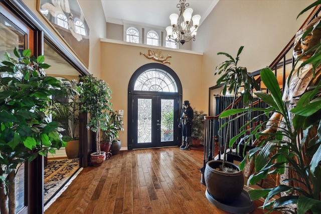 entryway featuring crown molding, an inviting chandelier, a high ceiling, wood-type flooring, and french doors