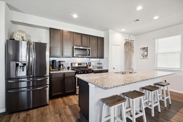 kitchen featuring backsplash, a breakfast bar, an island with sink, and appliances with stainless steel finishes