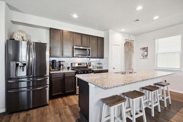 kitchen featuring a kitchen island with sink, dark hardwood / wood-style flooring, a kitchen breakfast bar, and appliances with stainless steel finishes