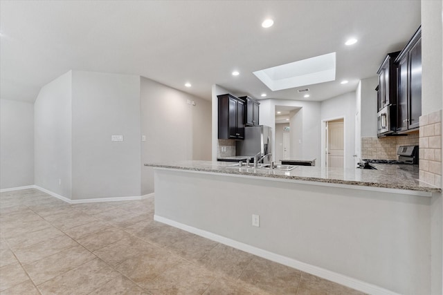 kitchen featuring sink, a skylight, kitchen peninsula, stainless steel appliances, and light stone countertops