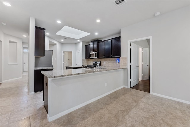 kitchen featuring appliances with stainless steel finishes, a skylight, tasteful backsplash, kitchen peninsula, and light stone countertops