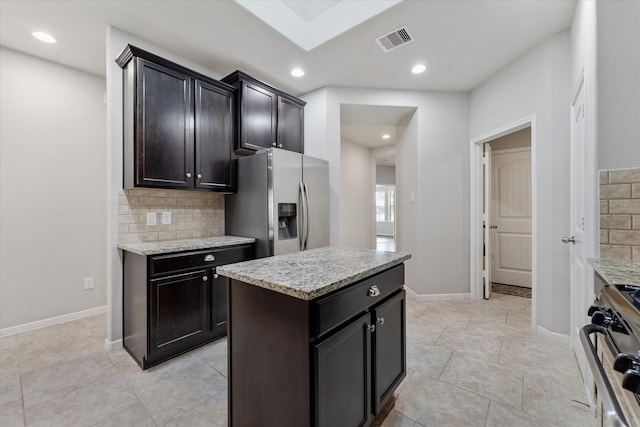 kitchen with stainless steel refrigerator with ice dispenser, light stone counters, a kitchen island, stove, and backsplash