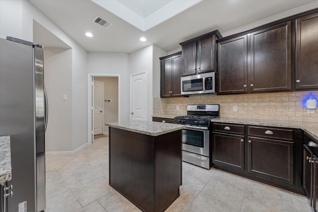 kitchen with dark brown cabinetry, light stone counters, appliances with stainless steel finishes, a kitchen island, and decorative backsplash