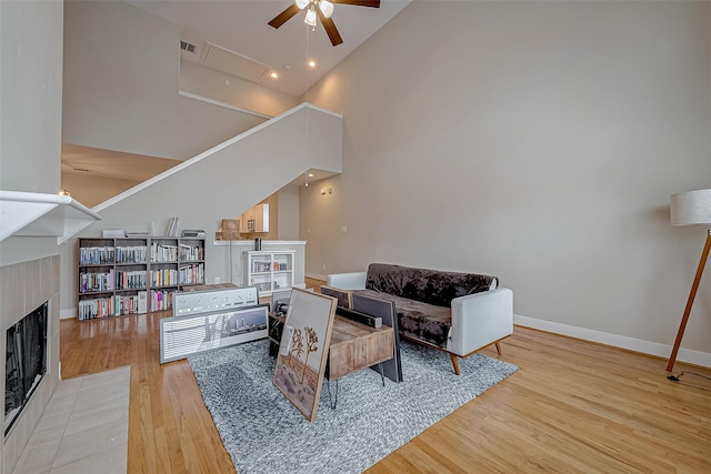 living room featuring ceiling fan, a towering ceiling, hardwood / wood-style floors, and a fireplace