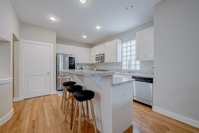 kitchen with stainless steel appliances, a kitchen island, white cabinets, and a kitchen breakfast bar