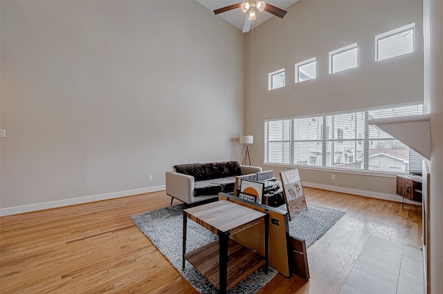 living room with a towering ceiling, light hardwood / wood-style flooring, and ceiling fan