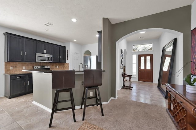 kitchen with sink, a breakfast bar area, appliances with stainless steel finishes, a kitchen island with sink, and backsplash