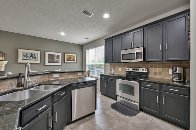 kitchen with sink, tasteful backsplash, light tile patterned floors, dark stone countertops, and appliances with stainless steel finishes