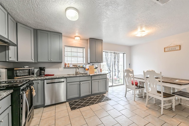 kitchen with light stone counters, sink, gray cabinets, and appliances with stainless steel finishes