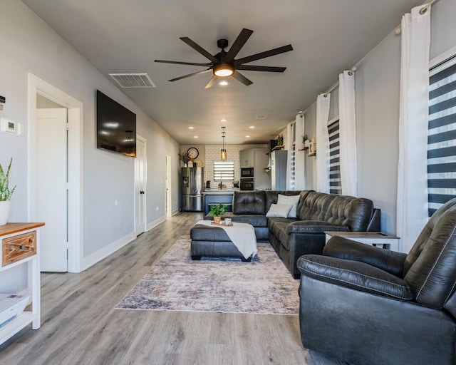 living room with light hardwood / wood-style floors, ceiling fan, and brick wall