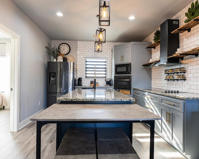 kitchen with pendant lighting, a kitchen island with sink, tasteful backsplash, black appliances, and light hardwood / wood-style floors