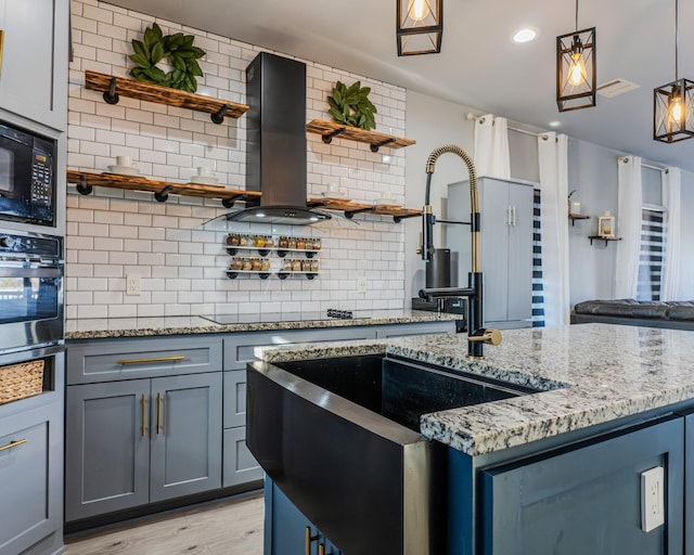 kitchen featuring backsplash, hanging light fixtures, black appliances, light stone countertops, and wall chimney exhaust hood