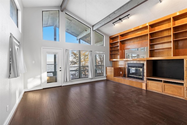 unfurnished living room with beam ceiling, a towering ceiling, dark wood-type flooring, and rail lighting