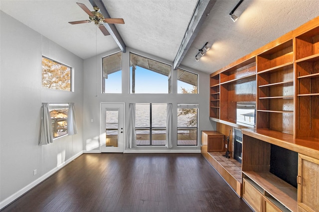 unfurnished living room with dark hardwood / wood-style floors, rail lighting, vaulted ceiling with beams, and a textured ceiling