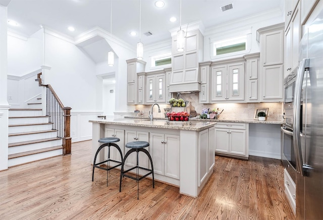 kitchen featuring hanging light fixtures, ornamental molding, a kitchen island with sink, and light stone counters