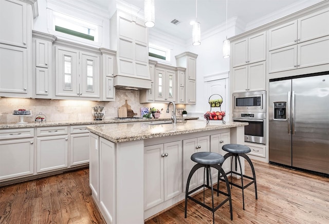 kitchen featuring pendant lighting, sink, crown molding, stainless steel appliances, and a center island with sink