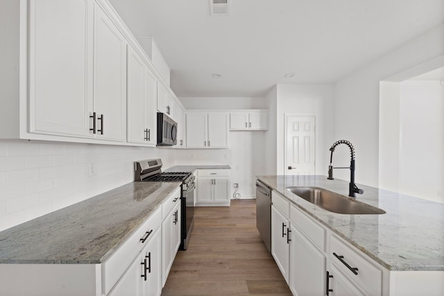 kitchen with appliances with stainless steel finishes, white cabinetry, an island with sink, sink, and light stone counters