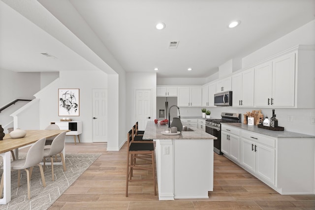 kitchen with a kitchen island with sink, light stone counters, white cabinetry, and appliances with stainless steel finishes