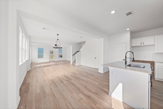 kitchen with hanging light fixtures, a kitchen island with sink, sink, and white cabinets