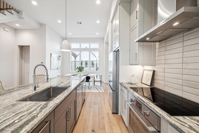 kitchen featuring sink, appliances with stainless steel finishes, light stone counters, decorative light fixtures, and wall chimney exhaust hood