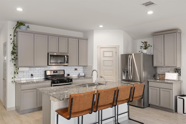 kitchen with sink, a breakfast bar, appliances with stainless steel finishes, a kitchen island with sink, and light stone counters