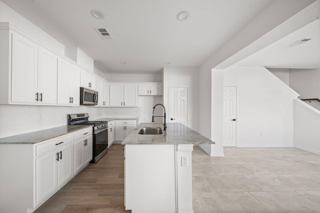 kitchen with sink, light stone counters, stainless steel appliances, a kitchen island with sink, and white cabinets