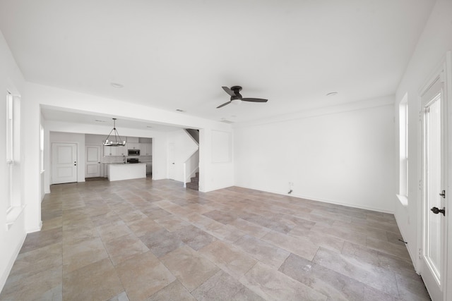 unfurnished living room featuring ceiling fan with notable chandelier