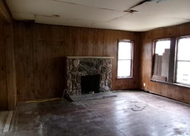 unfurnished living room featuring a stone fireplace and wood walls