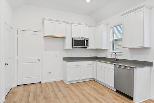 kitchen featuring sink, vaulted ceiling, appliances with stainless steel finishes, light hardwood / wood-style floors, and white cabinets