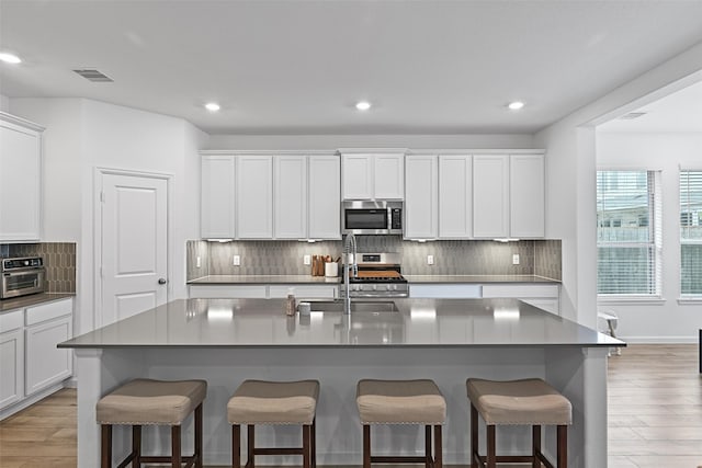 kitchen with white cabinetry, sink, stainless steel appliances, and an island with sink