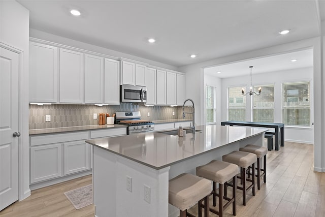 kitchen with stainless steel appliances, white cabinetry, sink, and a kitchen island with sink