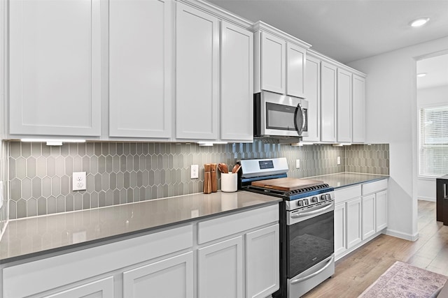 kitchen featuring stainless steel appliances, backsplash, white cabinets, and light wood-type flooring