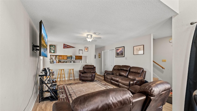 living room with ceiling fan, a textured ceiling, and light wood-type flooring