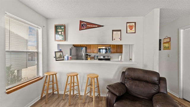 kitchen with a breakfast bar, a textured ceiling, kitchen peninsula, stainless steel appliances, and hardwood / wood-style floors