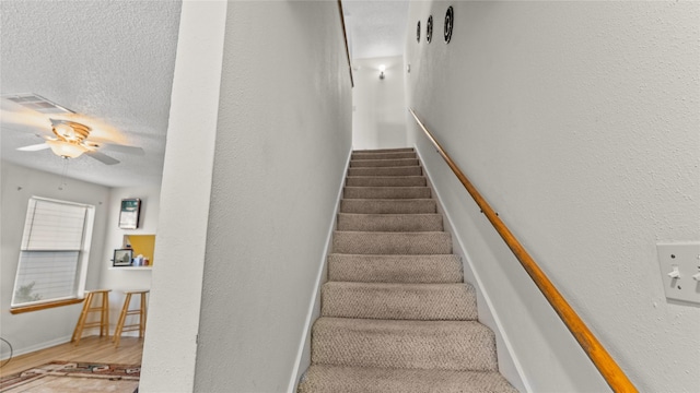 stairway with a textured ceiling and ceiling fan