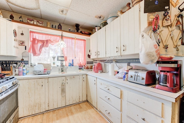 kitchen featuring a drop ceiling, white cabinetry, pendant lighting, and range with gas stovetop