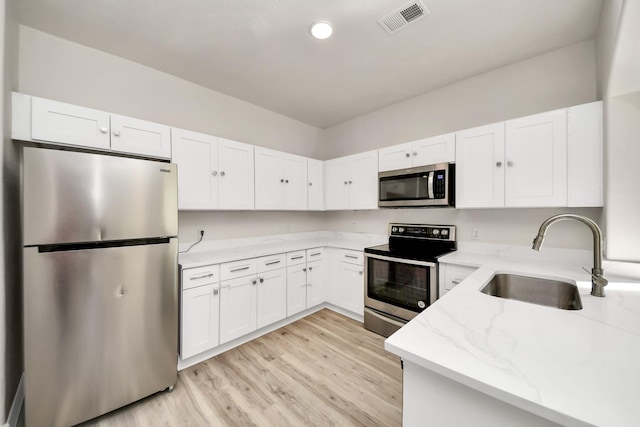 kitchen with white cabinetry, sink, light stone counters, light hardwood / wood-style floors, and stainless steel appliances