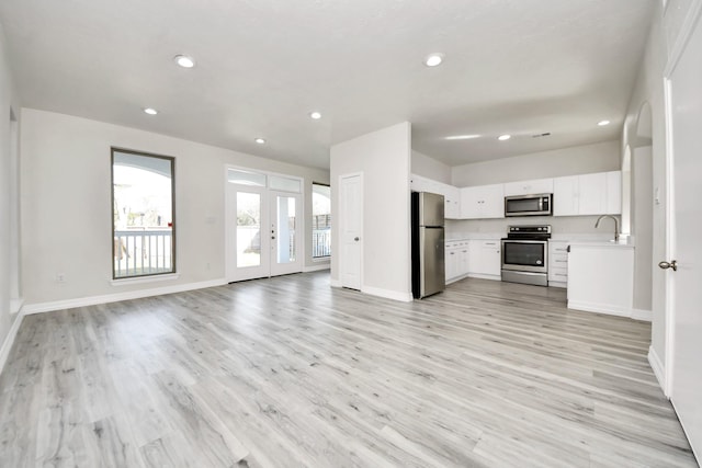 unfurnished living room featuring french doors, sink, and light hardwood / wood-style floors