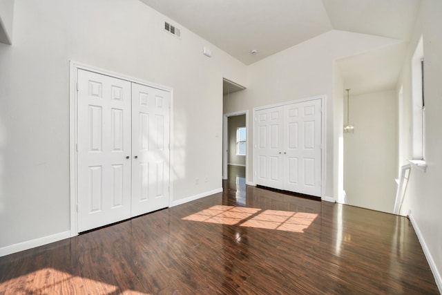 unfurnished bedroom featuring dark hardwood / wood-style floors, two closets, and high vaulted ceiling