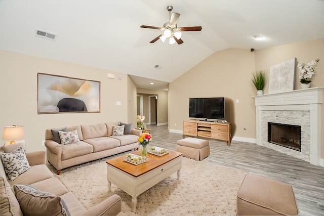 living room with lofted ceiling, a stone fireplace, light hardwood / wood-style flooring, and ceiling fan