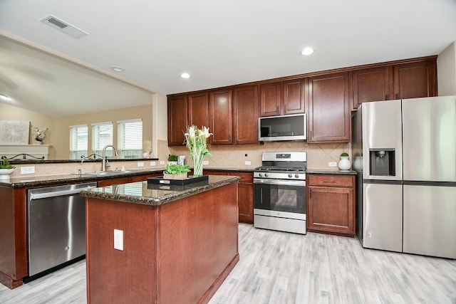 kitchen with appliances with stainless steel finishes, sink, decorative backsplash, dark stone counters, and a center island