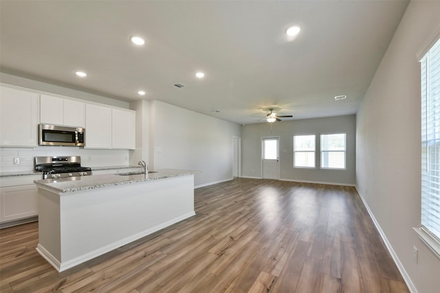 kitchen with sink, white cabinetry, light hardwood / wood-style flooring, stainless steel appliances, and a kitchen island with sink