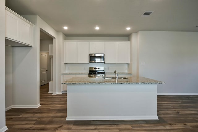 kitchen featuring appliances with stainless steel finishes, light stone countertops, a center island with sink, and white cabinets