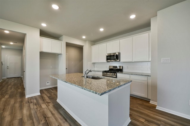 kitchen featuring sink, white cabinetry, stainless steel appliances, a center island with sink, and dark stone counters