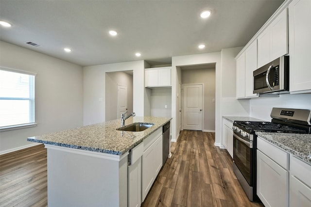 kitchen with appliances with stainless steel finishes, white cabinetry, sink, light stone counters, and a center island with sink